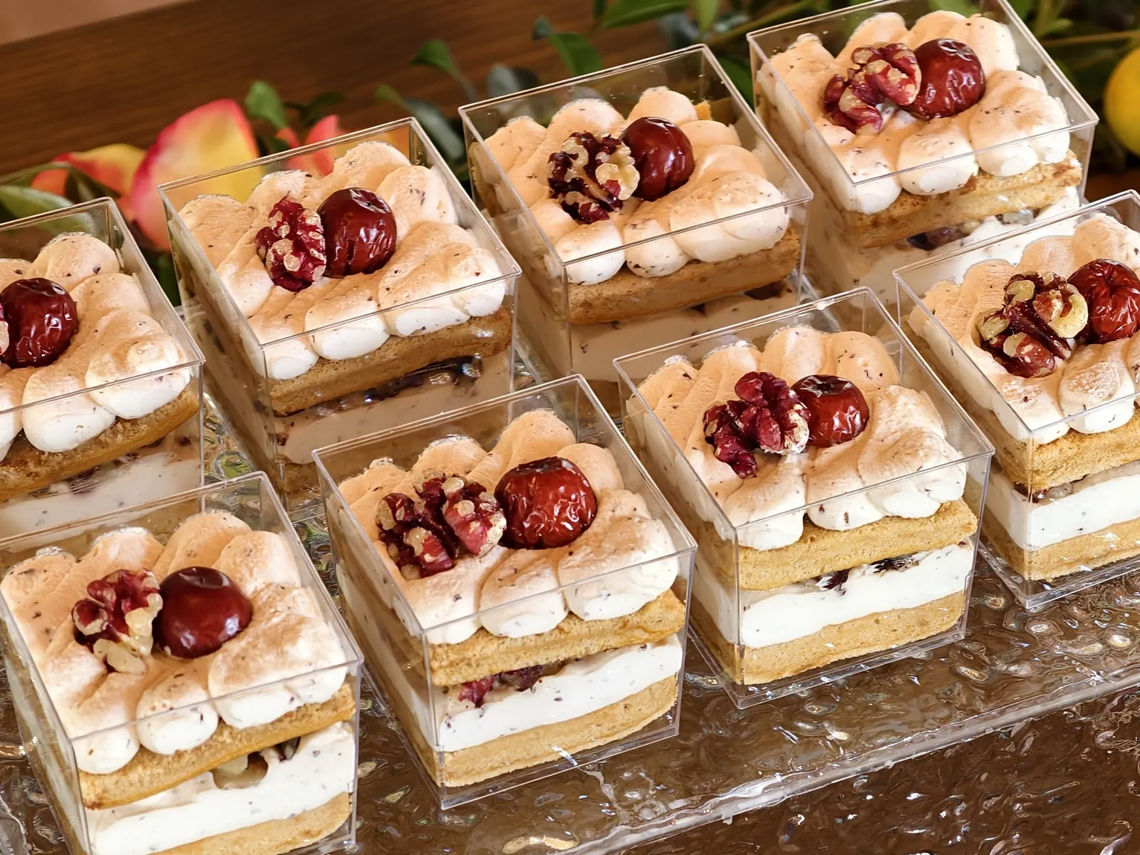 Square dessert cups layered with sponge and cream, topped with piped cream, walnuts and red dates, on a glass tray