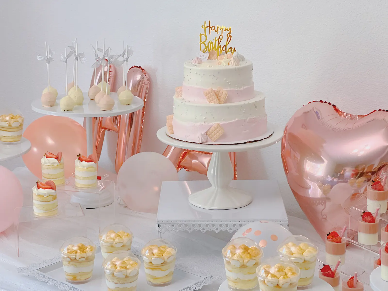 Pink-themed dessert table with a tiered cake and heart balloons