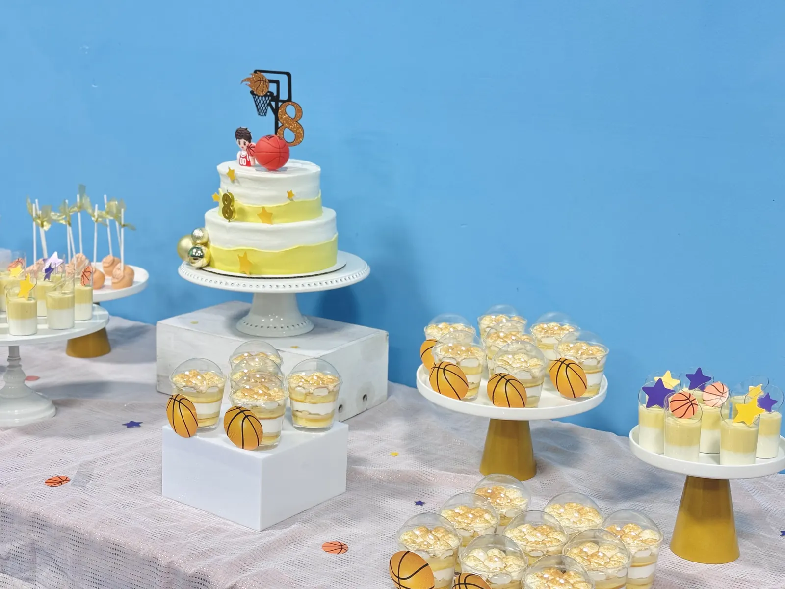 Tiered cake and cupcakes on stands against a blue backdrop