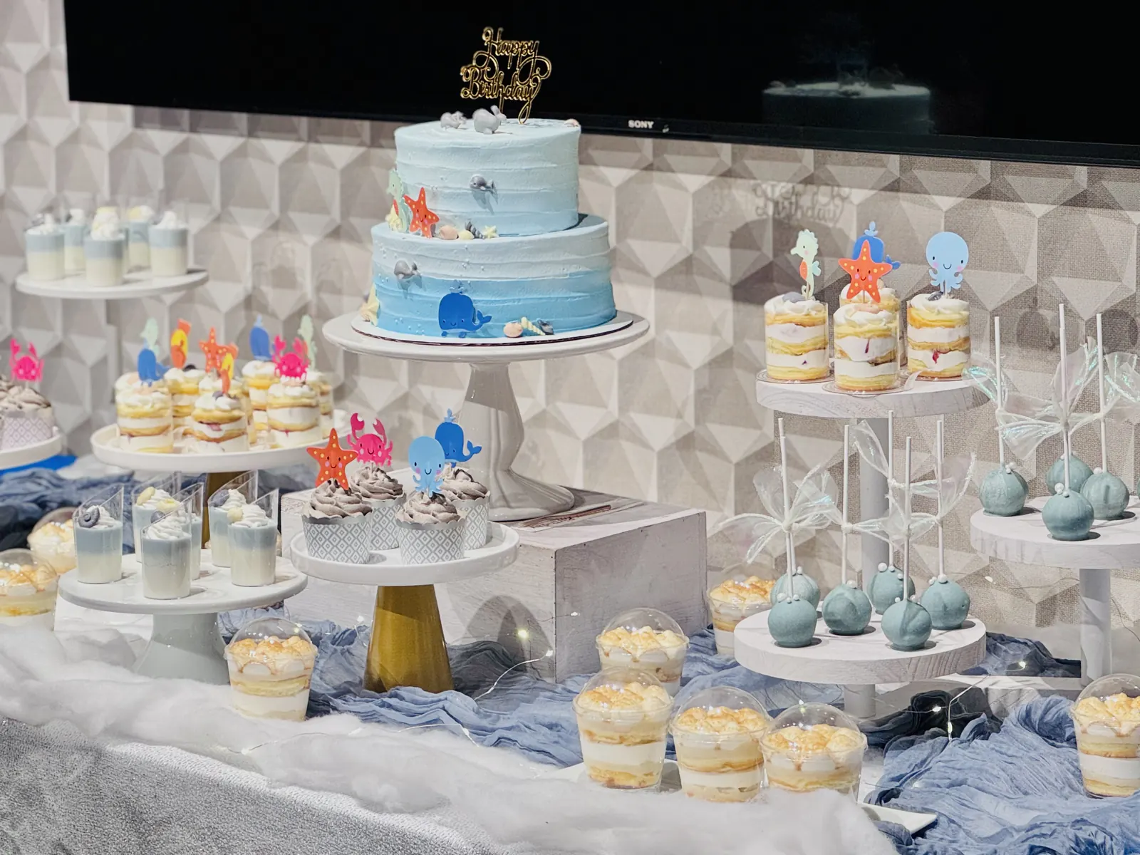 Light blue dessert table with a tiered cake and cupcakes