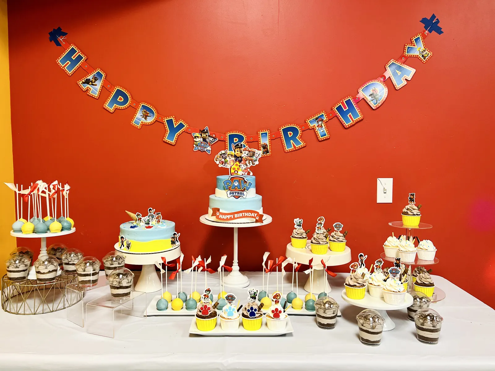 Birthday dessert table with banner against a red wall